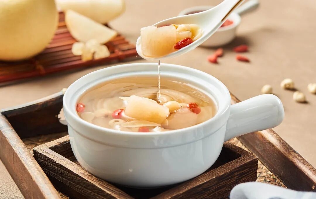 A steaming bowl of snow pear and lily bulb soup with fresh snow pears beside it